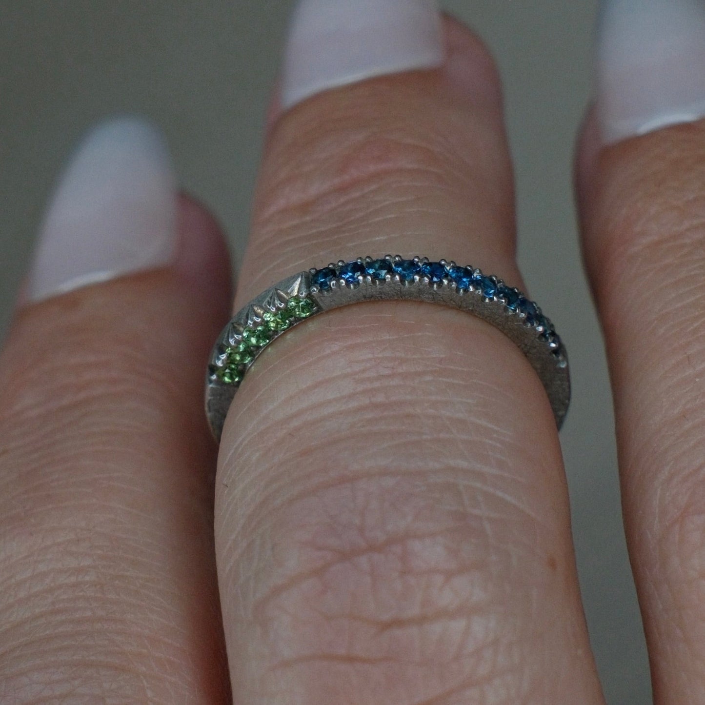 Close-up of a hand wearing a silver ring with blue and green gemstones.